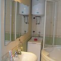 łazienka - umywalka Koło; szklany, półkolisty parawan wanny częściowo otwarty